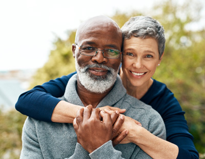 Senior woman hugging senior man from behind