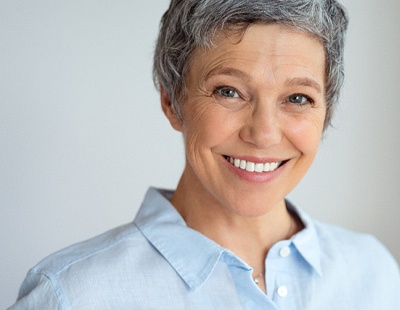 A middle-aged woman wearing a button-down shirt and smiling after receiving her dental crowns in Aspen Hill