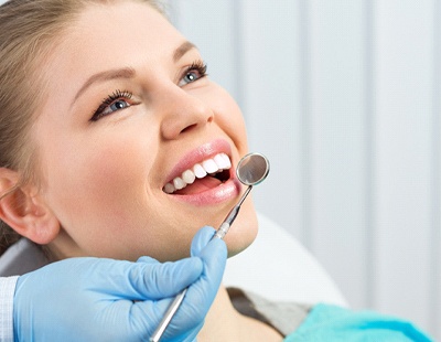 A young woman smiling with her mouth open while a dentist prepares to examine her smile