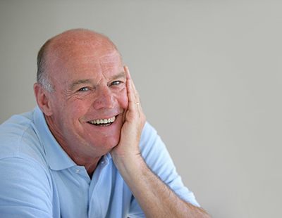 An older man wearing a blue shirt and smiling