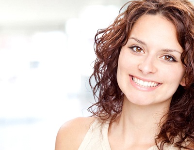 A young woman with dark, curly hair smiling after completing treatment with FastBraces® in Aspen Hill