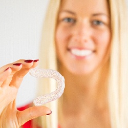 Woman with blonde hair holding a clear aligner with focus on aligner