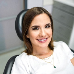Woman with brown hair sitting in dental chair smiling while looking at camera