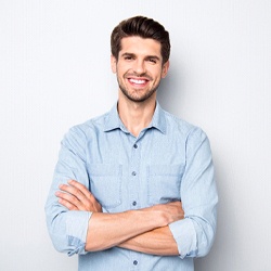 Man in blue collared shirt smiling with arms crossed