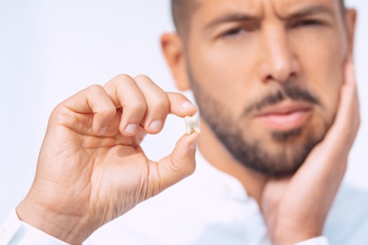 Man holding dislodged tooth and touching jaw in pain