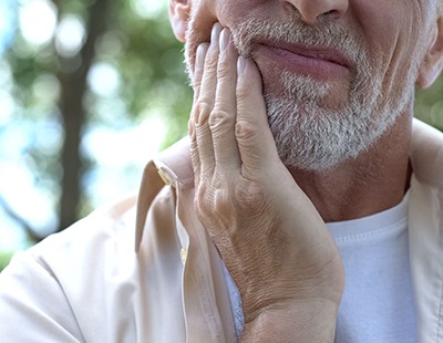 Man outside rubbing jaw in pain in need of dental implant salvage in Aspen Hill, MD