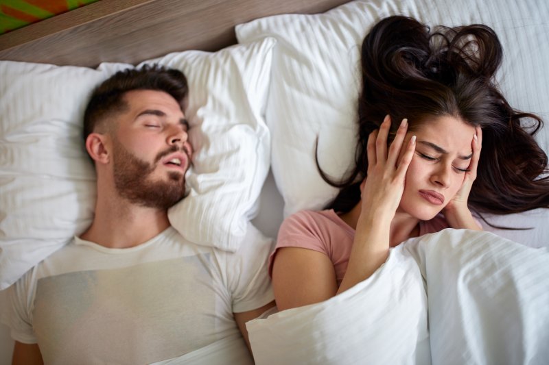 A woman in bed with her snoring husband